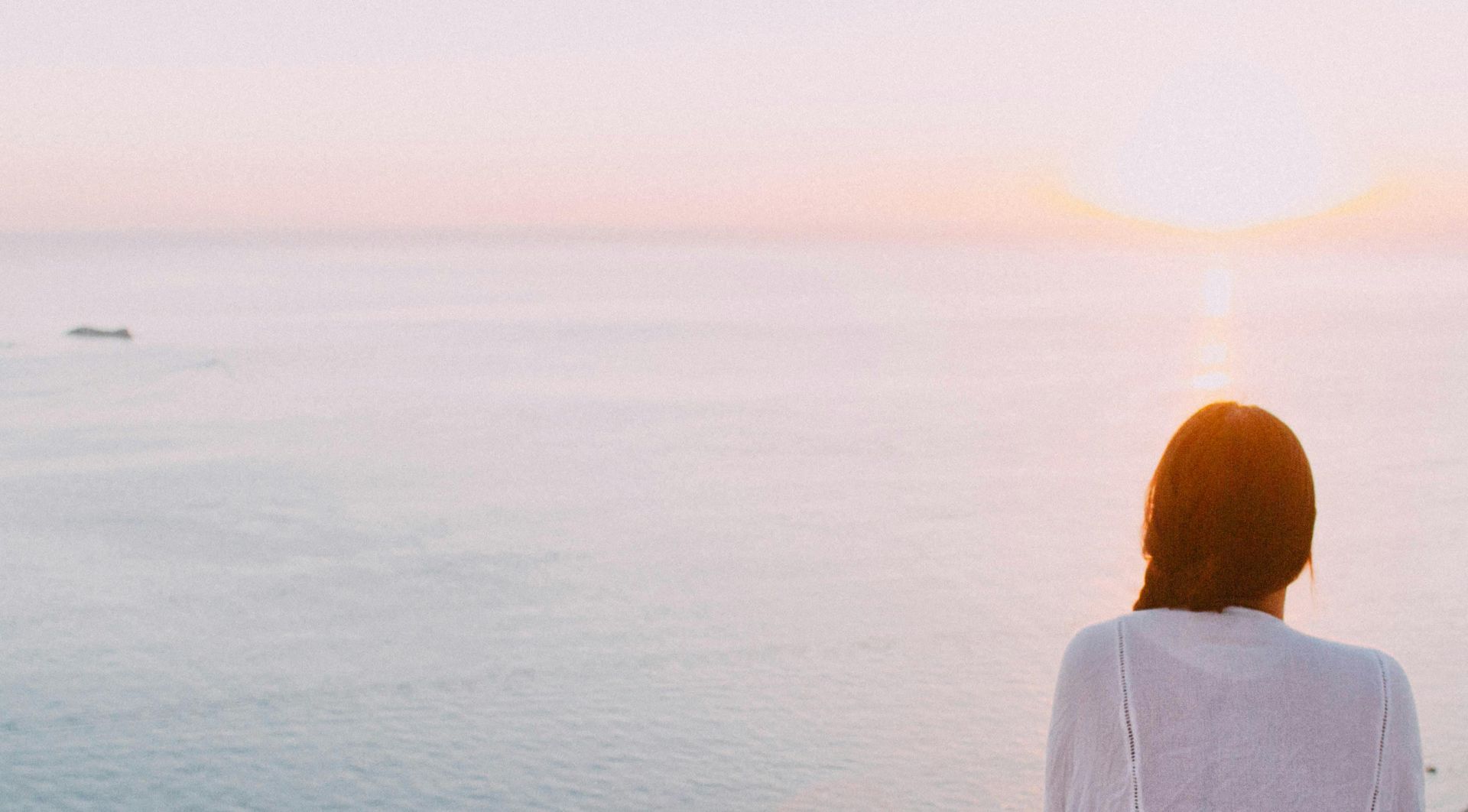 Woman Sitting on Gray Rock Near Body of Water