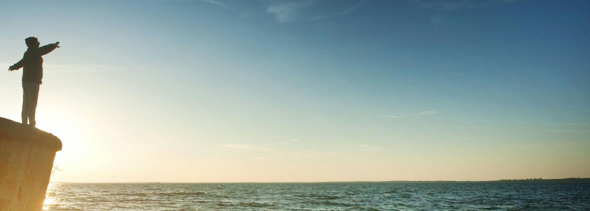 Silhouette of Person on Cliff Beside Body of Water during Golden Hour