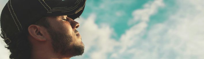 Man Wearing Black Cap With Eyes Closed Under Cloudy Sky